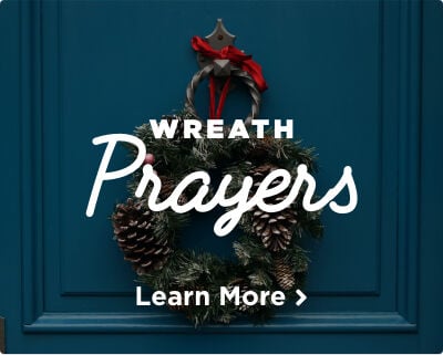 An Advent wreath decorated with a vibrant red bow and pinecones, hanging on a blue door. Image links to Advent Wreath Prayers page.